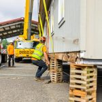 The crane crew secures a modular school building in preparation for moving it into place.