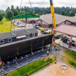 One half of a modular classroom being guided into place by the Omega Morgan crane services crew.
