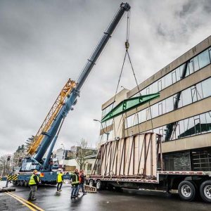 Omega Morgan crane services crew helps omega morgan machinery moving crew lift a mural outside a building