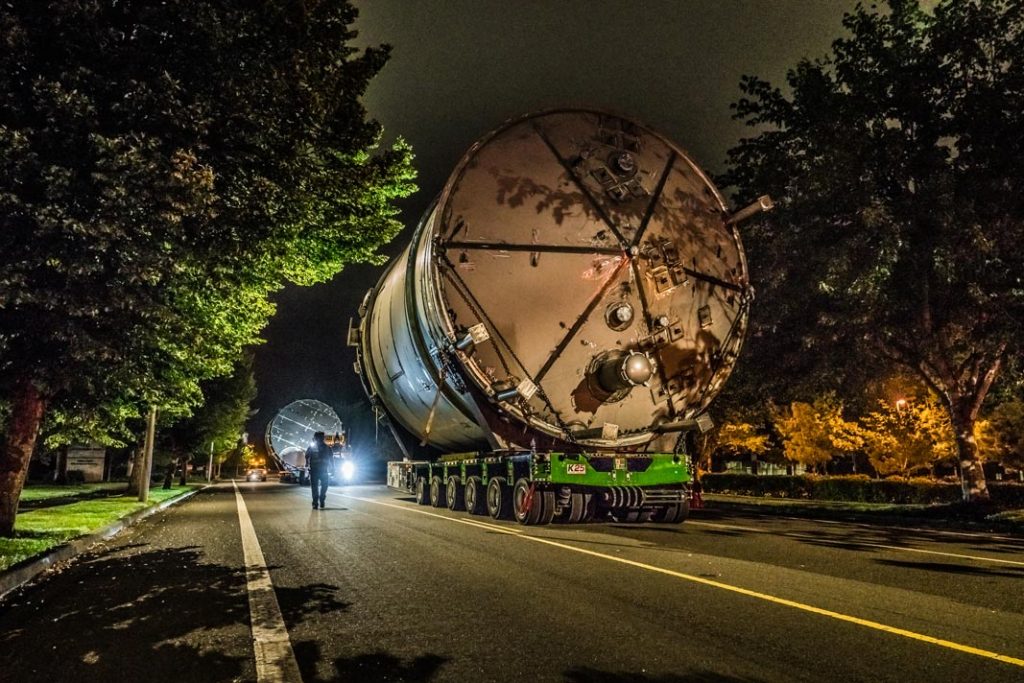 Omega Morgan Specialized transportation team transporting a twenty two foot wide ozone tank down a narrow road with trees on either side