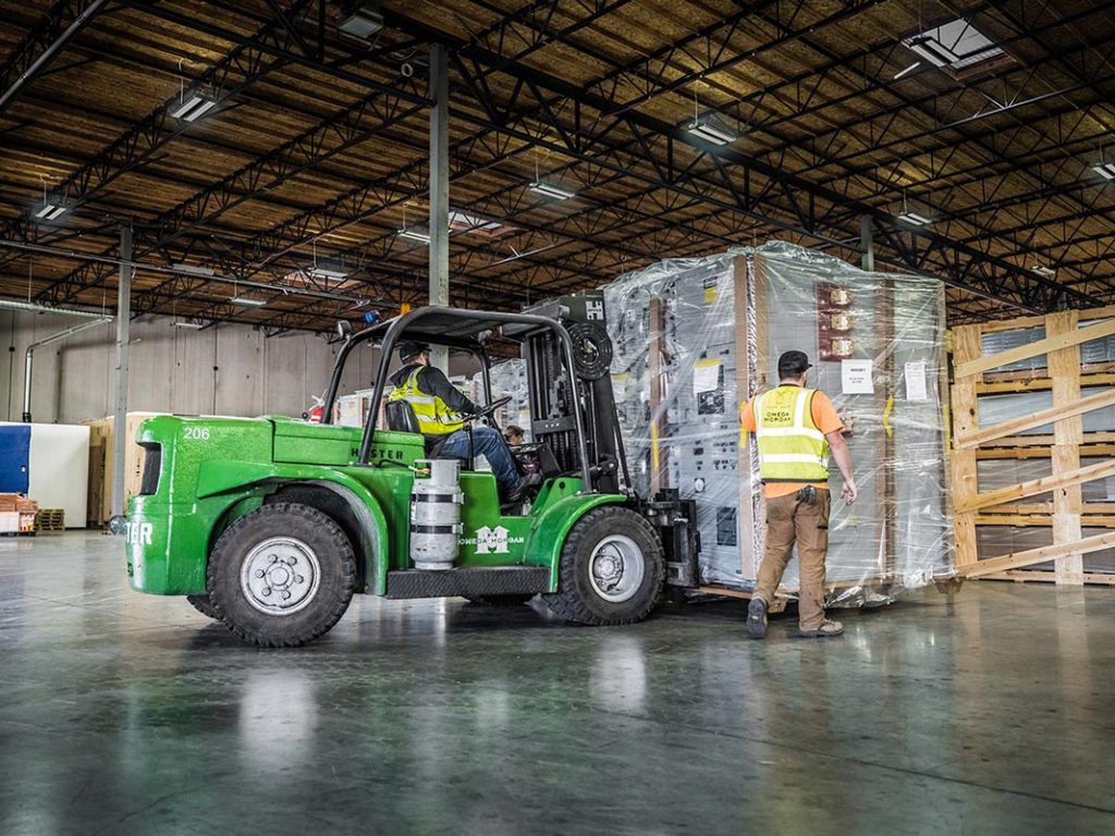 Omega Morgan workers bring a large piece of equipment into the Hillsboro warehouse and storage facility with a forklift