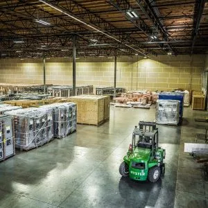 wide angle view of the inside of an Omega Morgan warehouse and storage facility with rows of large equipment being stored alongside a warehouse forklift