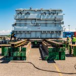 Crew members use a jack and slide system to move a transformer and load it onto the trailer.