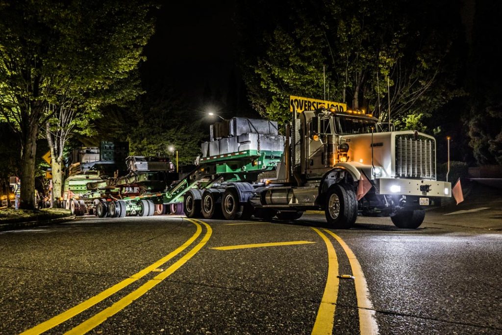 A Kenworth C500 prime mover at the front of a transformer load safely passing through an area of low clearance.